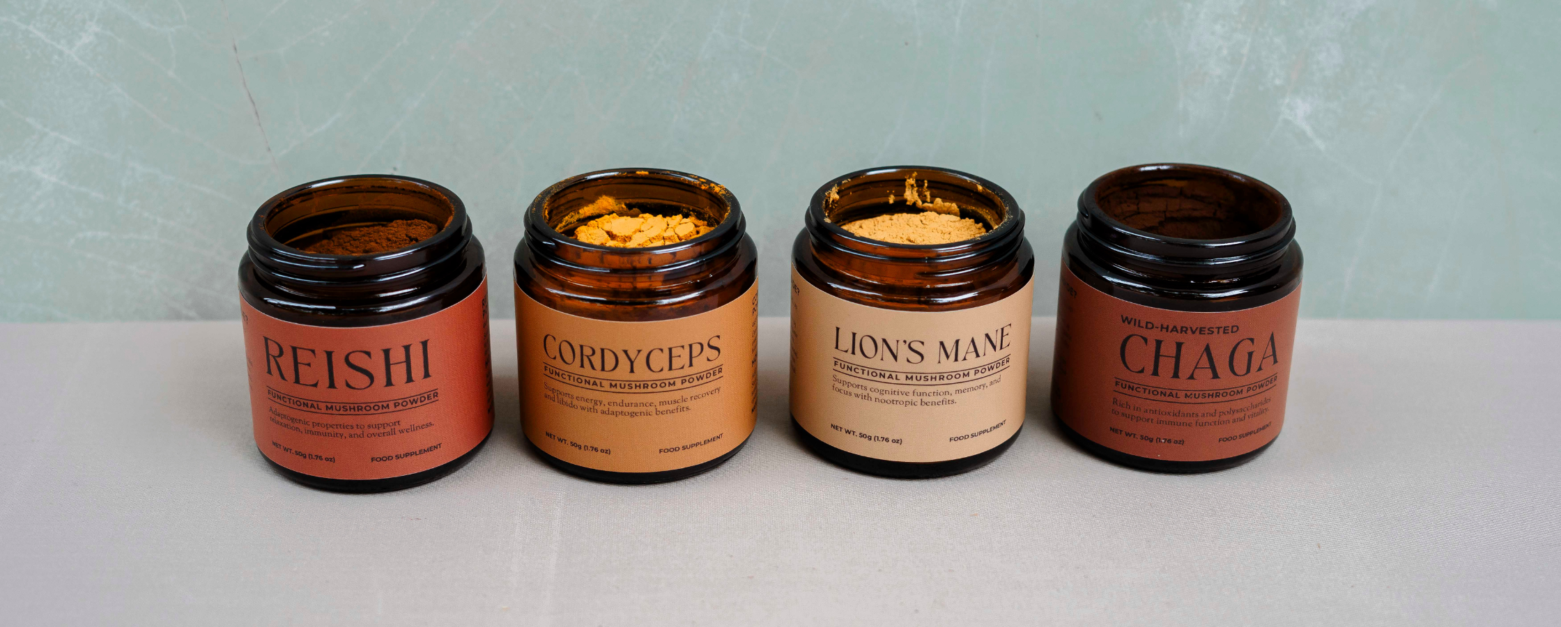 Four open amber glass jars of Nature’s Antidote functional mushroom extract powders—Reishi, Cordyceps, Lion’s Mane, and Chaga—showing their rich, earthy colors and fine textures against a neutral background.