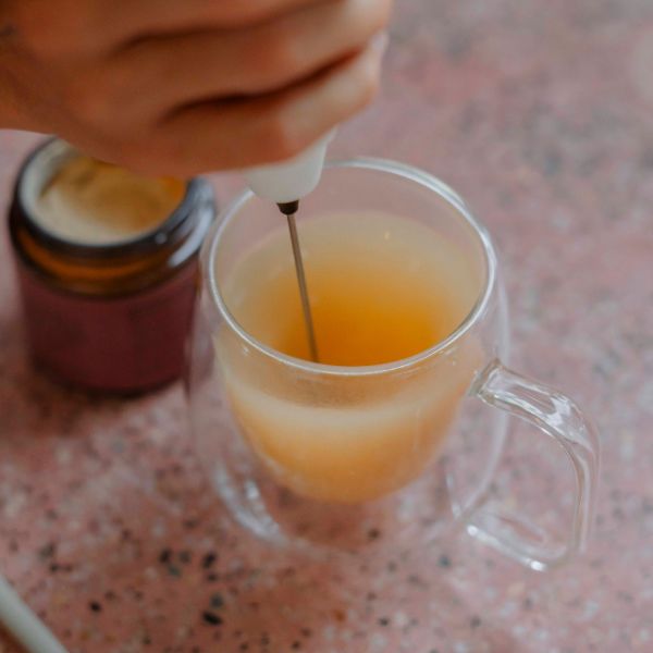 Ashwagandha drink being whisked in a clear glass mug with an electric frother, creating a smooth and creamy texture.