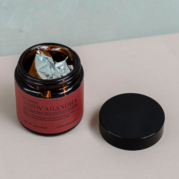 A glass jar of ashwagandha powder with the lid off shows a sealed aluminium bag that keeps the powder secure and fresh.