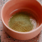 A close-up of vibrant green matcha powder sifted into a pink ceramic bowl, showcasing its smooth and finely milled texture.